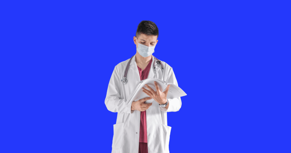 Um médico jovem, usando jaleco branco, máscara cirúrgica e um estetoscópio roxo ao redor do pescoço, está de pé e lendo um prontuário ou livro aberto que segura com as duas mãos. Ele tem cabelo escuro curto e está olhando para baixo, concentrado na leitura. O fundo é azul liso.