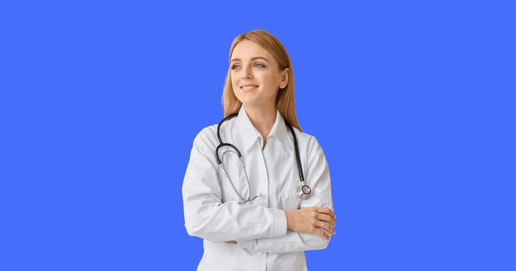 Uma médica loira sorri e olha para o lado, com os braços cruzados e um estetoscópio em seu pescoço.