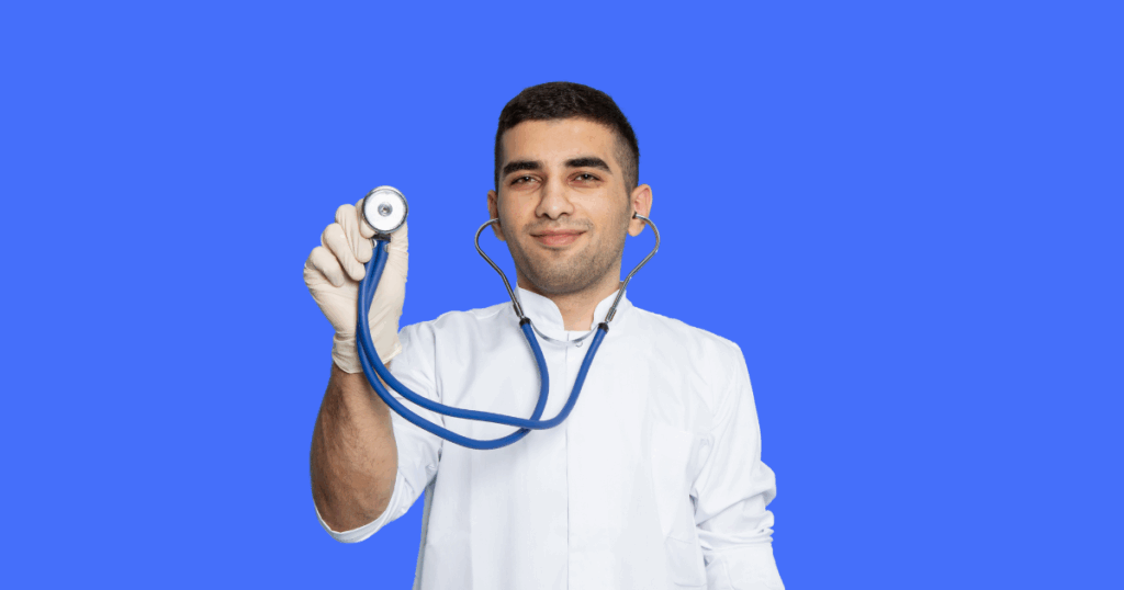 Um médico jovem, usando jaleco branco e luvas, segura um estetoscópio azul em direção à câmera, sorrindo.