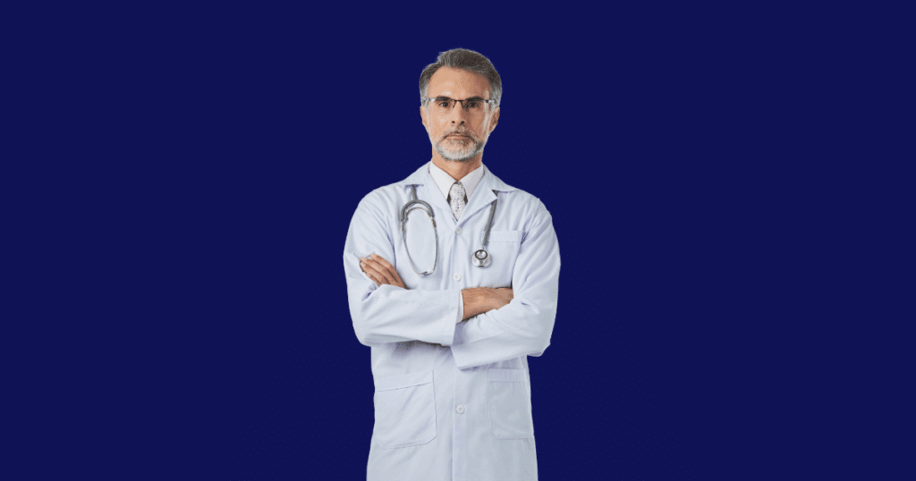 Médico de meia-idade com jaleco branco, óculos e estetoscópio no pescoço, de braços cruzados, em frente a um fundo azul escuro.