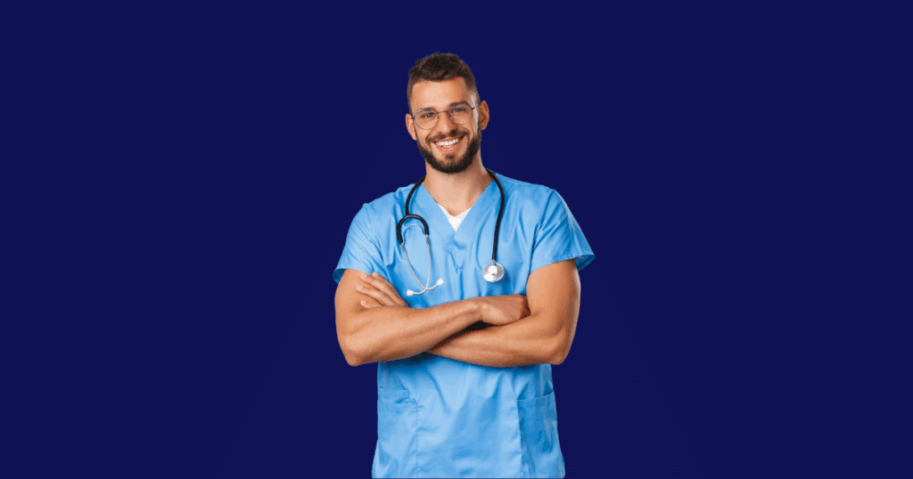 Médico jovem sorrindo com os braços cruzados, vestindo jaleco azul e estetoscópio no pescoço, posicionado sobre fundo azul escuro.