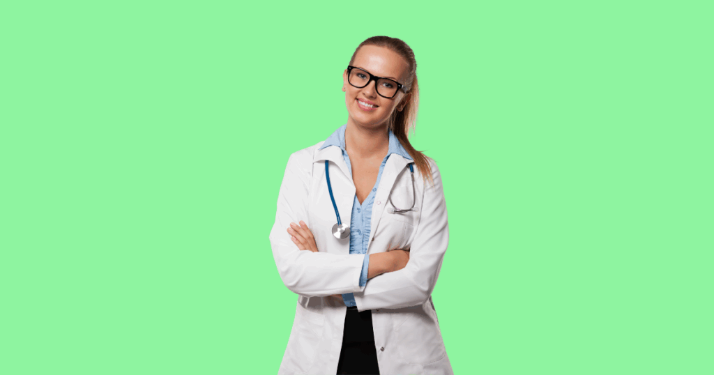 Médica jovem de cabelos presos, usando óculos e jaleco branco com estetoscópio no pescoço, sorrindo com os braços cruzados diante de um fundo verde-claro.