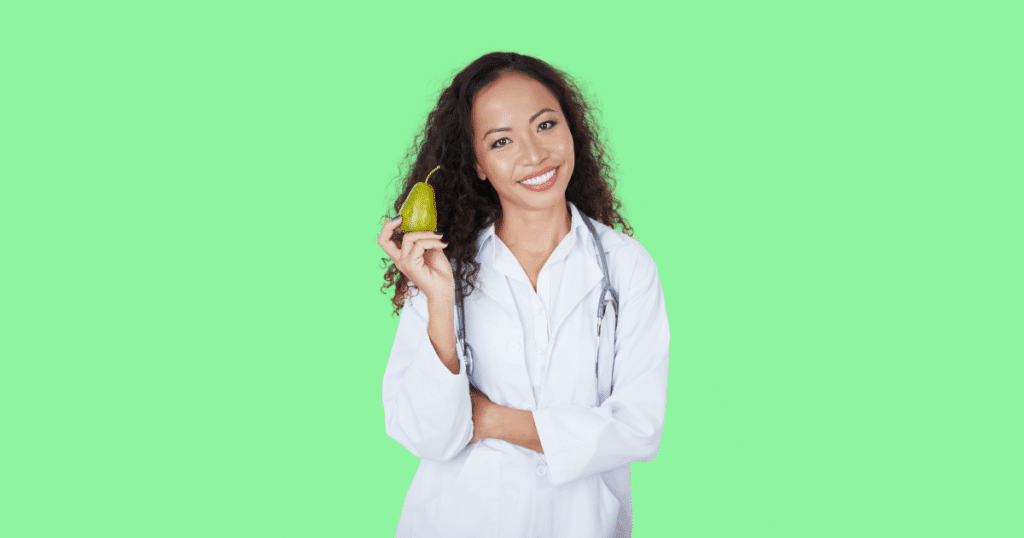 Nutricionista sorridente com jaleco branco e estetoscópio segura uma pera sobre fundo verde claro, representando saúde, alimentação equilibrada e bem-estar