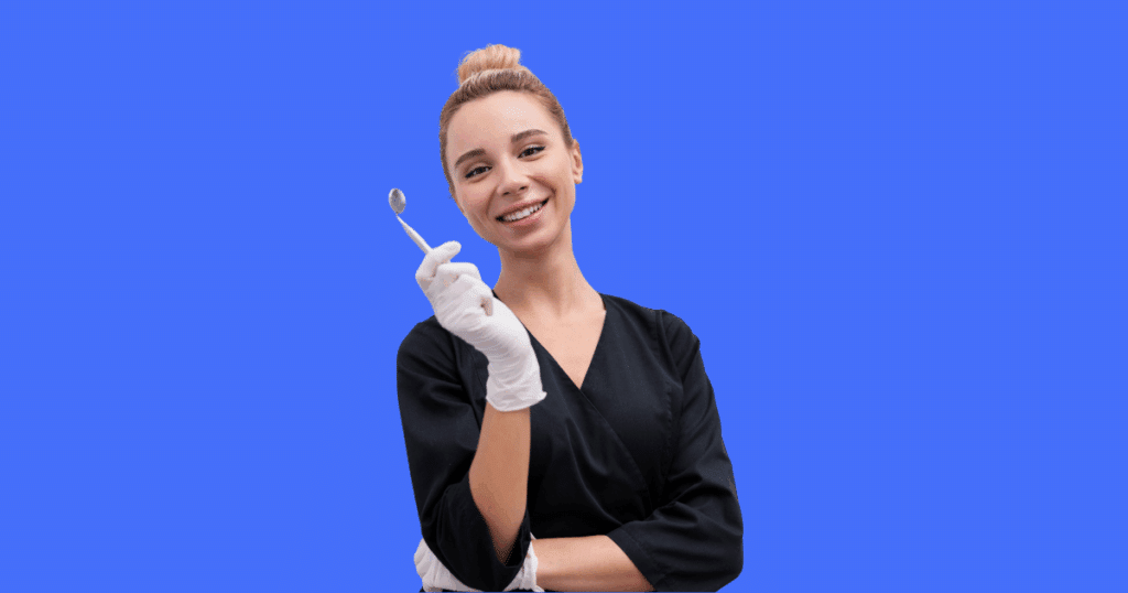 Dentista sorridente vestida de jaleco preto e luvas brancas segura um espelho odontológico, olhando para a câmera. Fundo azul sólido.