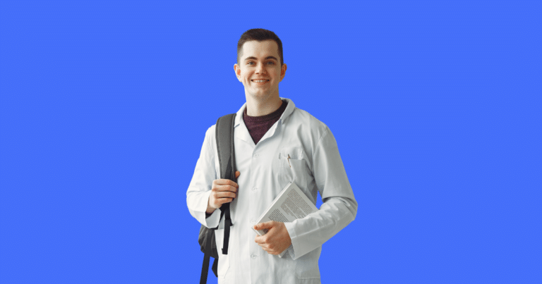 Estudante de medicina sorridente vestindo jaleco branco segura um livro e usa mochila sobre um dos ombros. Fundo azul sólido. Imagem ilustrativa para conteúdo sobre as melhores e piores faculdades de Medicina segundo a nota do ENAMED.
